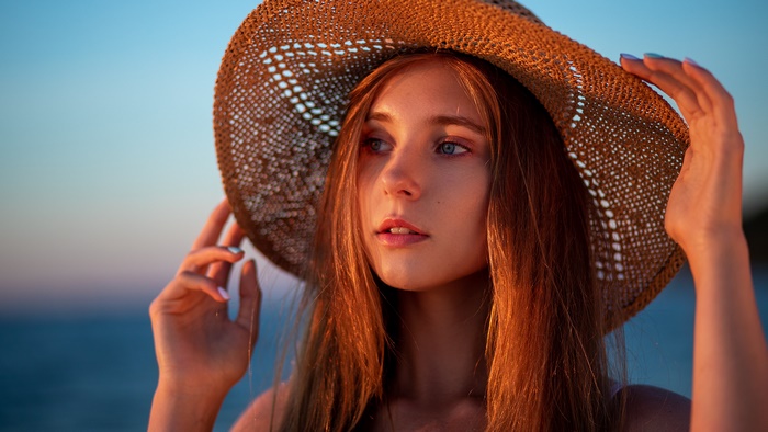 Young woman with a straw hat at sunset