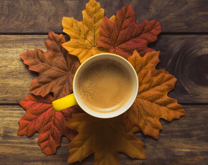 Coffee cup surrounded by autumn leaves on a wooden table
