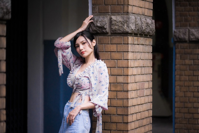 Asian woman with black hair leaning against a brick pillar