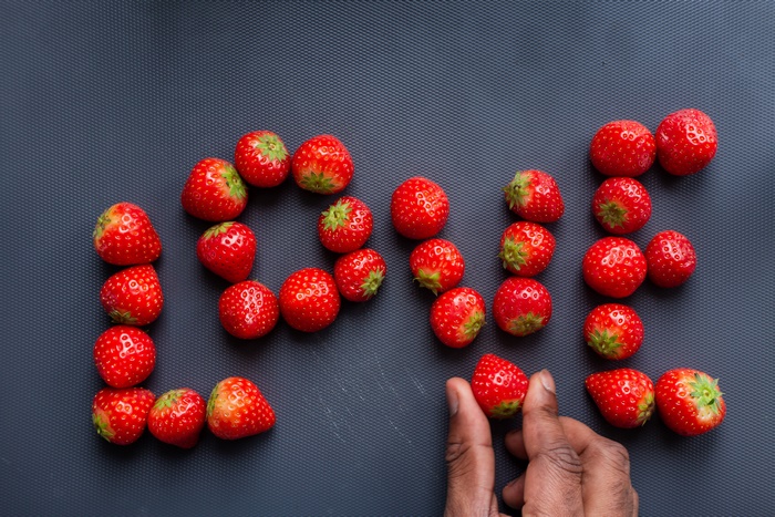 Love spelled with strawberries and a hand