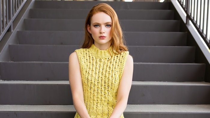 Sadie Sink in yellow knit top on stairs