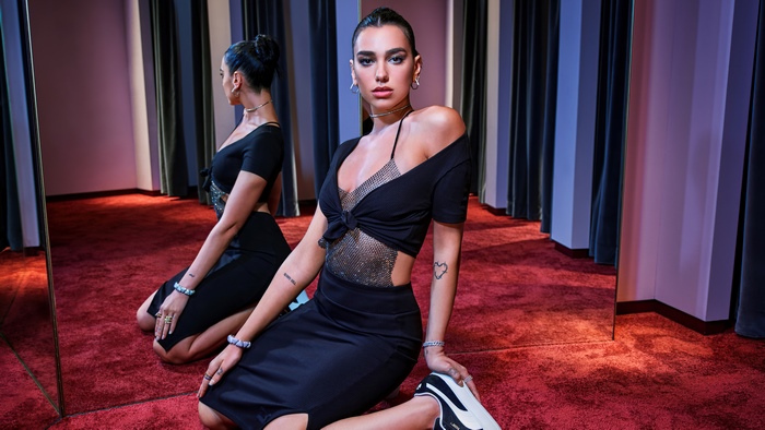 Dua Lipa in a black dress posing in a studio