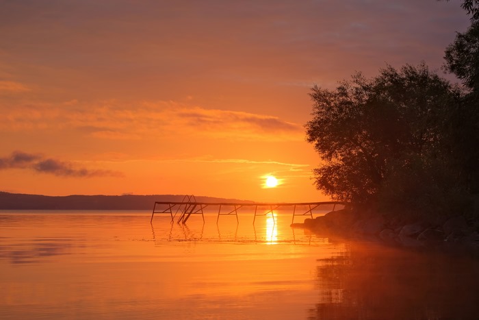 Sunset over a lake with a pier and trees