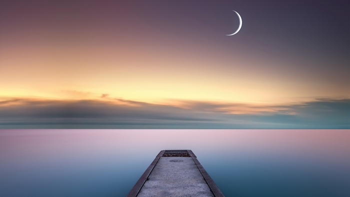 Crescent moon over a pier and ocean at sunset