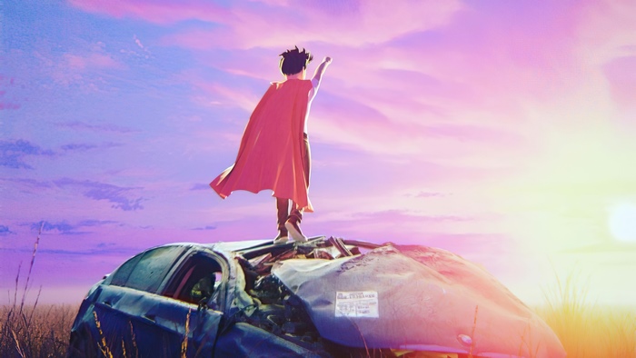Boy with red cape standing on wrecked car