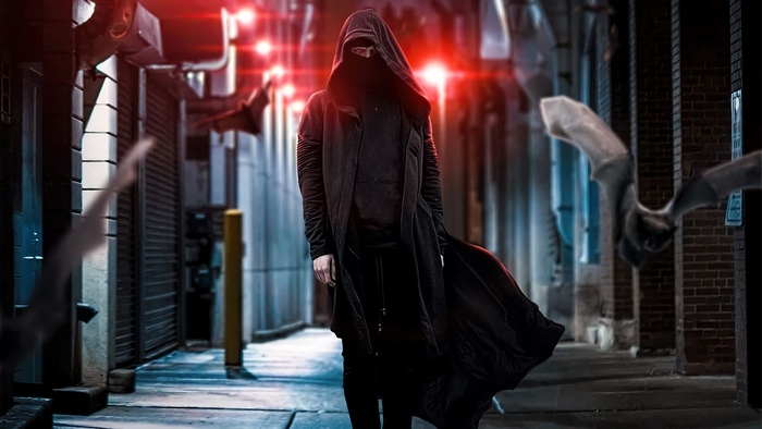 Person in dark hooded cloak in alley with bats