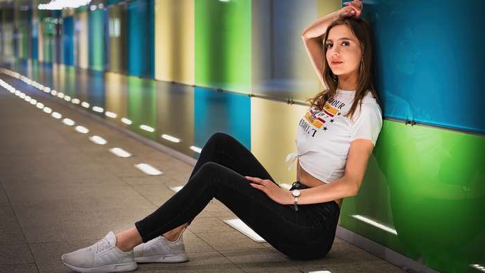 Girl in white t-shirt and black jeans sitting in colorful hallway