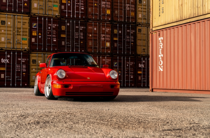 Red Porsche 911 parked near shipping containers