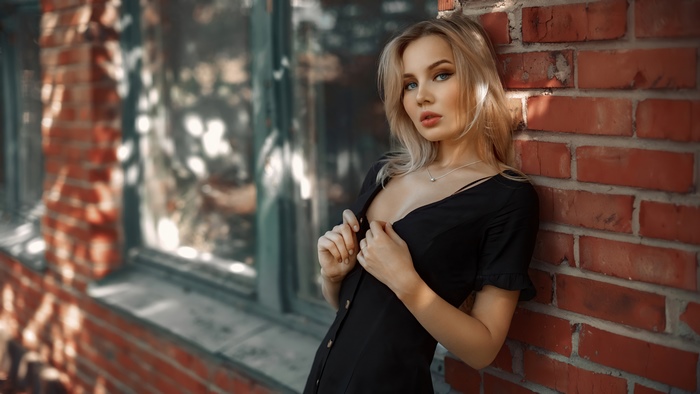 Blonde woman in black dress leaning against brick wall