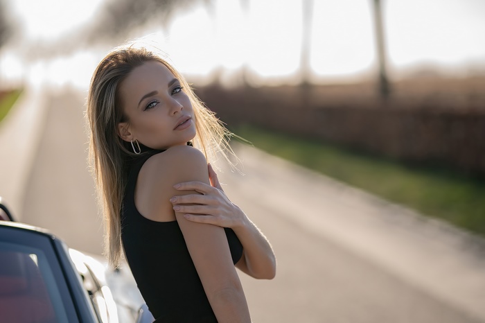 Blonde model in black dress near a car