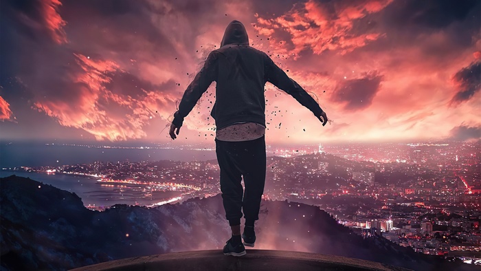 Man in hoodie on cliff overlooking city at sunset 4K