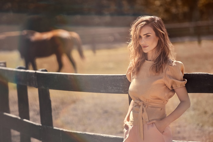 Woman in peach top and pants by a fence with horse
