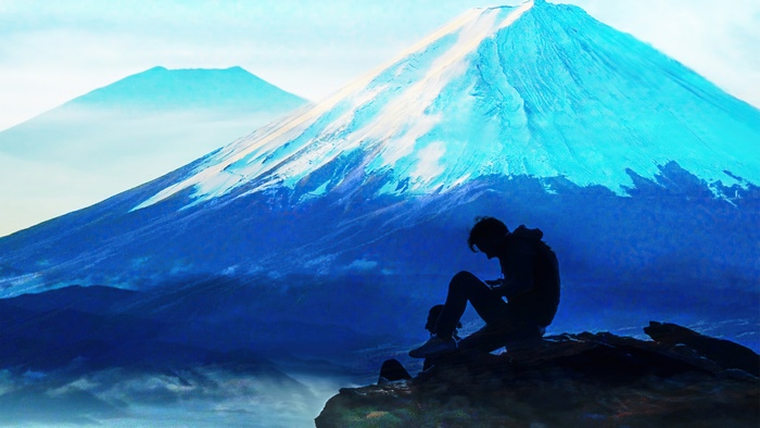 Silhouette of a person sitting on a rock with Mount Fuji in the background