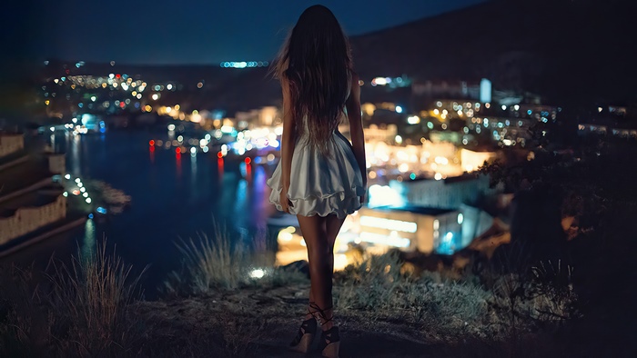 Girl in white dress overlooking city lights at night