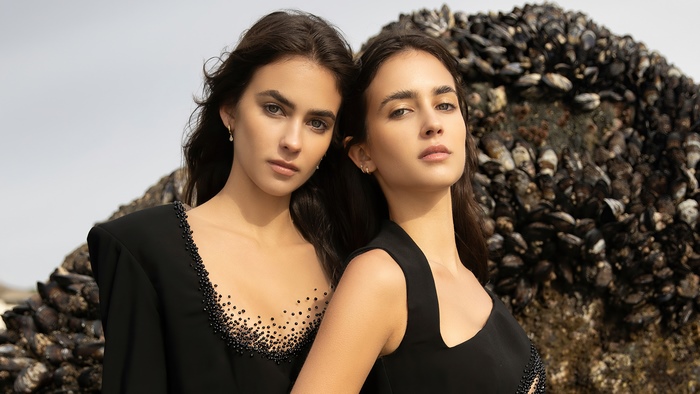 Two models in black dresses by the sea