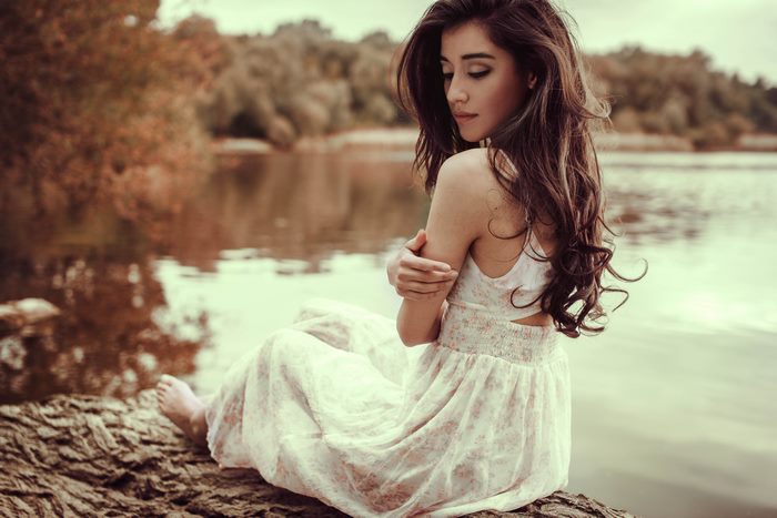 Woman in white dress sitting by a lake