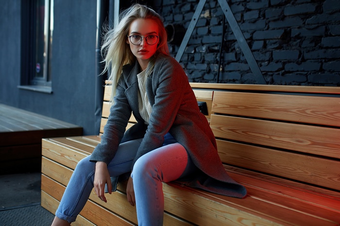 Blonde model wearing glasses and coat sitting on bench