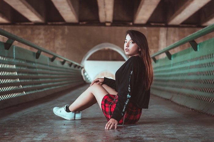 Girl in plaid skirt sitting under bridge