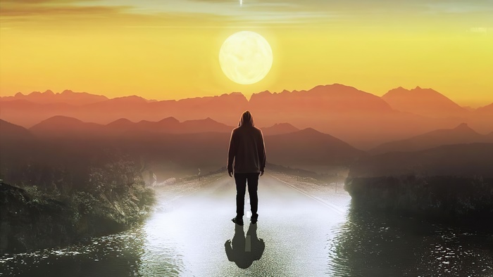 Person in hoodie standing on road at sunset