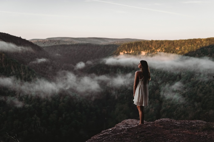 Girl in white dress on cliff overlooking foggy mountains