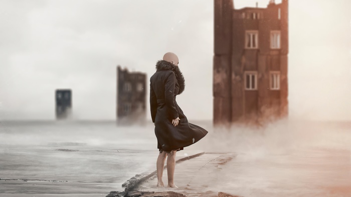 Bald person in black coat in foggy landscape with ruins