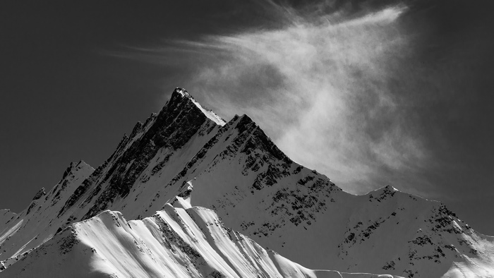 Monochrome snow-capped mountains with wispy clouds