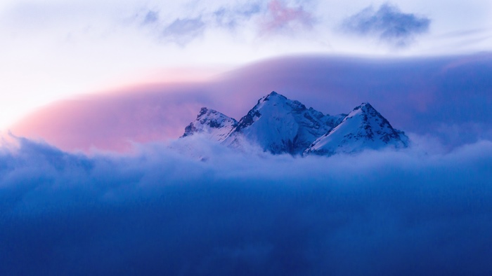 Snowy mountains emerge from clouds at sunrise