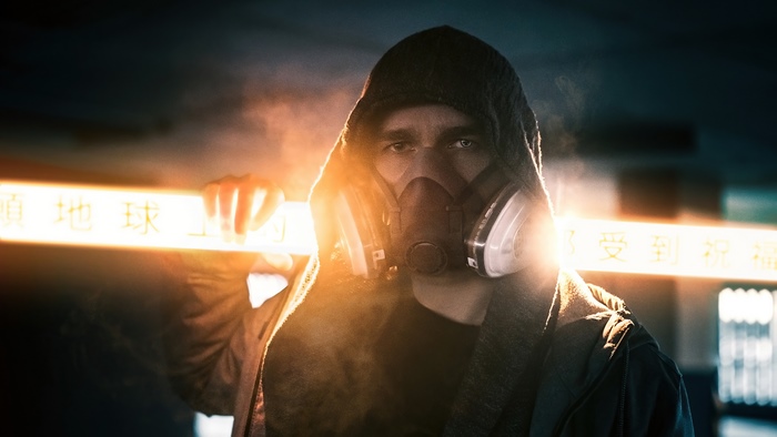 Man in gas mask and hoodie holding glowing sign