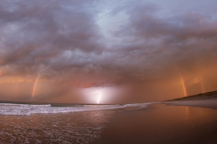 Lightning strike over ocean with double rainbow