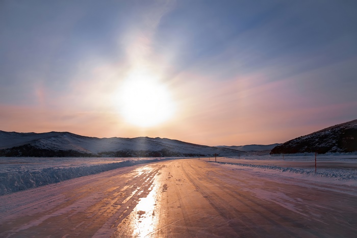 Frozen road through snowy mountains at sunset 4K