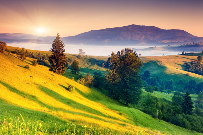 Sunrise over misty mountains and green hills