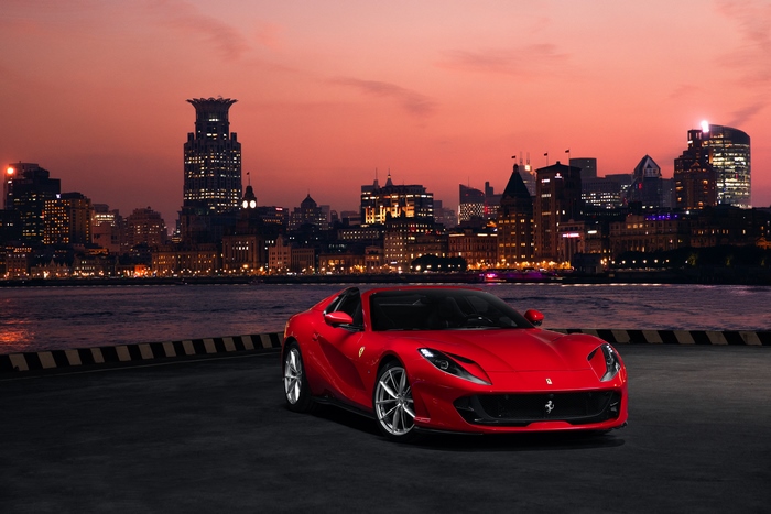 Red Ferrari 812 Superfast parked by a city skyline at dusk