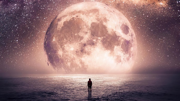 Man standing in water looking at giant moon and stars