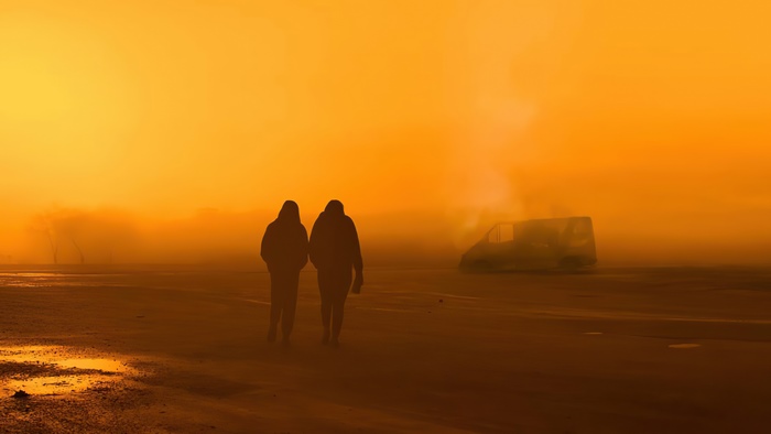Two people walking in a foggy orange landscape with a van