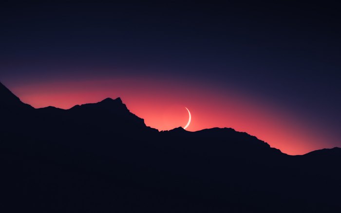 Crescent moon over silhouetted mountains at sunset