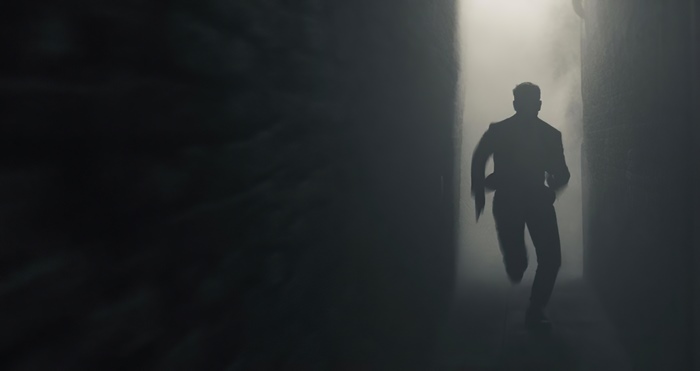Man in suit running through foggy alley