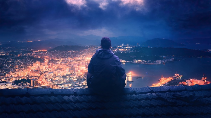 Man sitting on a rooftop overlooking a city at night