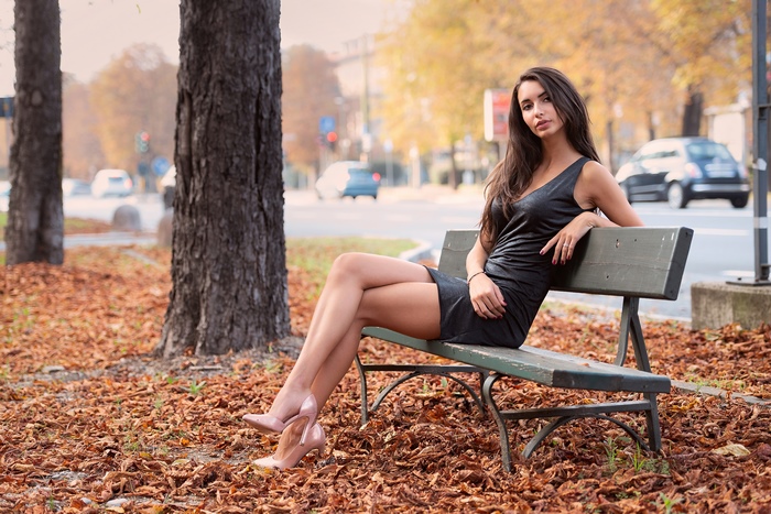 Woman in black dress sitting on a bench in autumn
