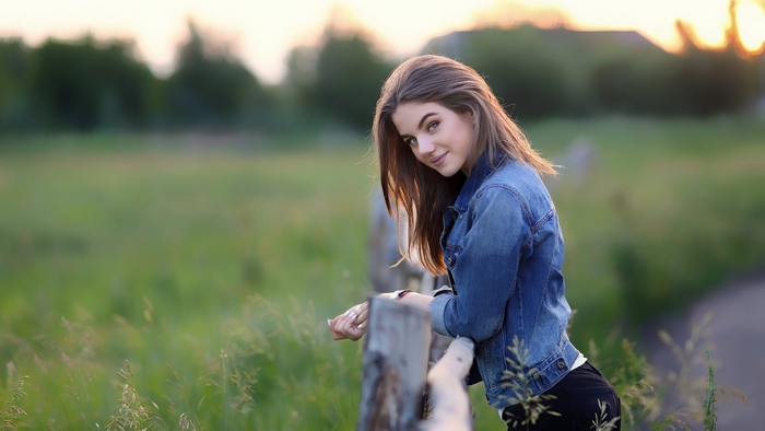 Girl in denim jacket leaning on fence