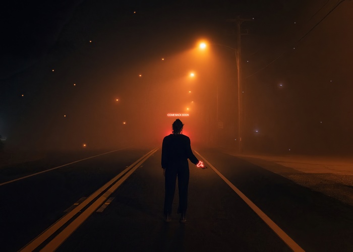 Person on foggy road with neon sign