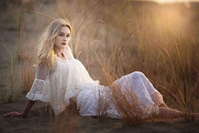 Blonde woman in white dress on sand dunes at sunset