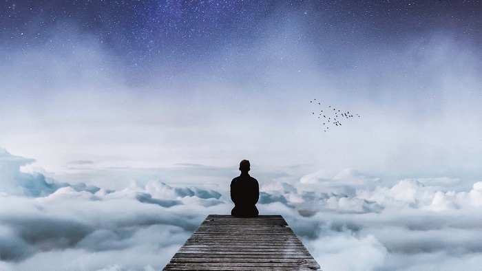 Silhouette of a person meditating on a pier above clouds under a starry sky
