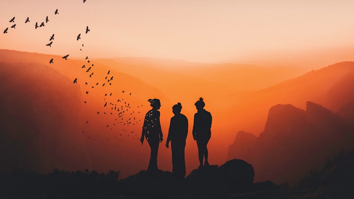 Three figures silhouetted against an orange sunset with birds flying