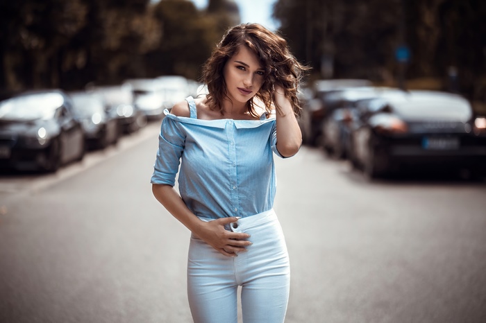 Model with curly hair in a blue shirt and white pants