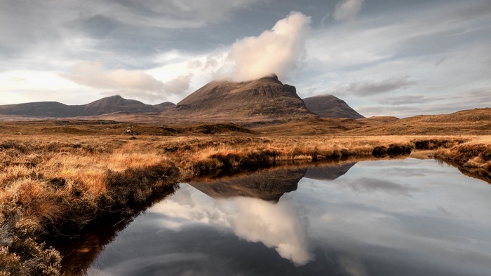 Mountains reflected in a calm lake under a cloudy sky