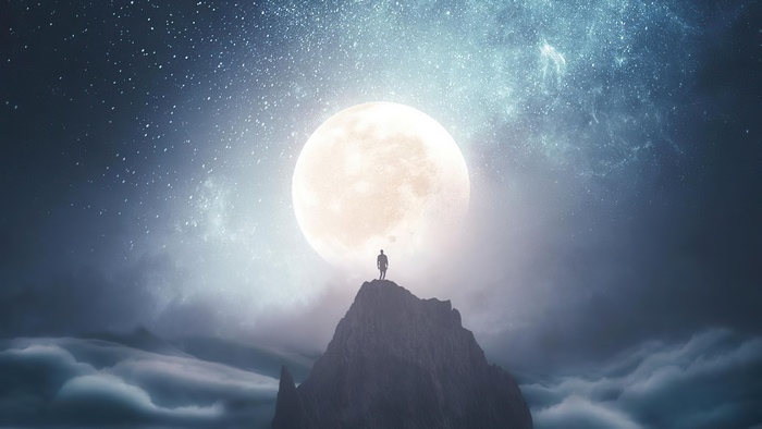 Man on mountain peak under large moon and stars
