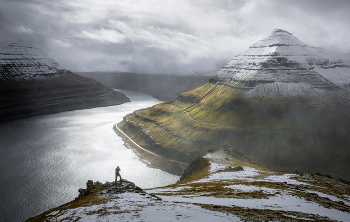Man on cliff overlooking fjord and mountains