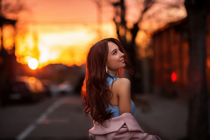 Woman in blue top and pink coat at sunset
