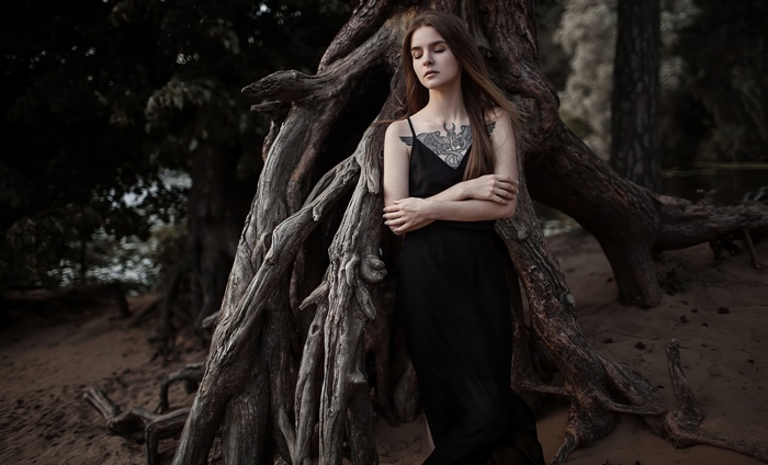 Girl with tattoo in black dress near tree roots