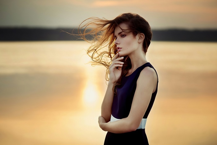 Woman in dark dress by the water at sunset